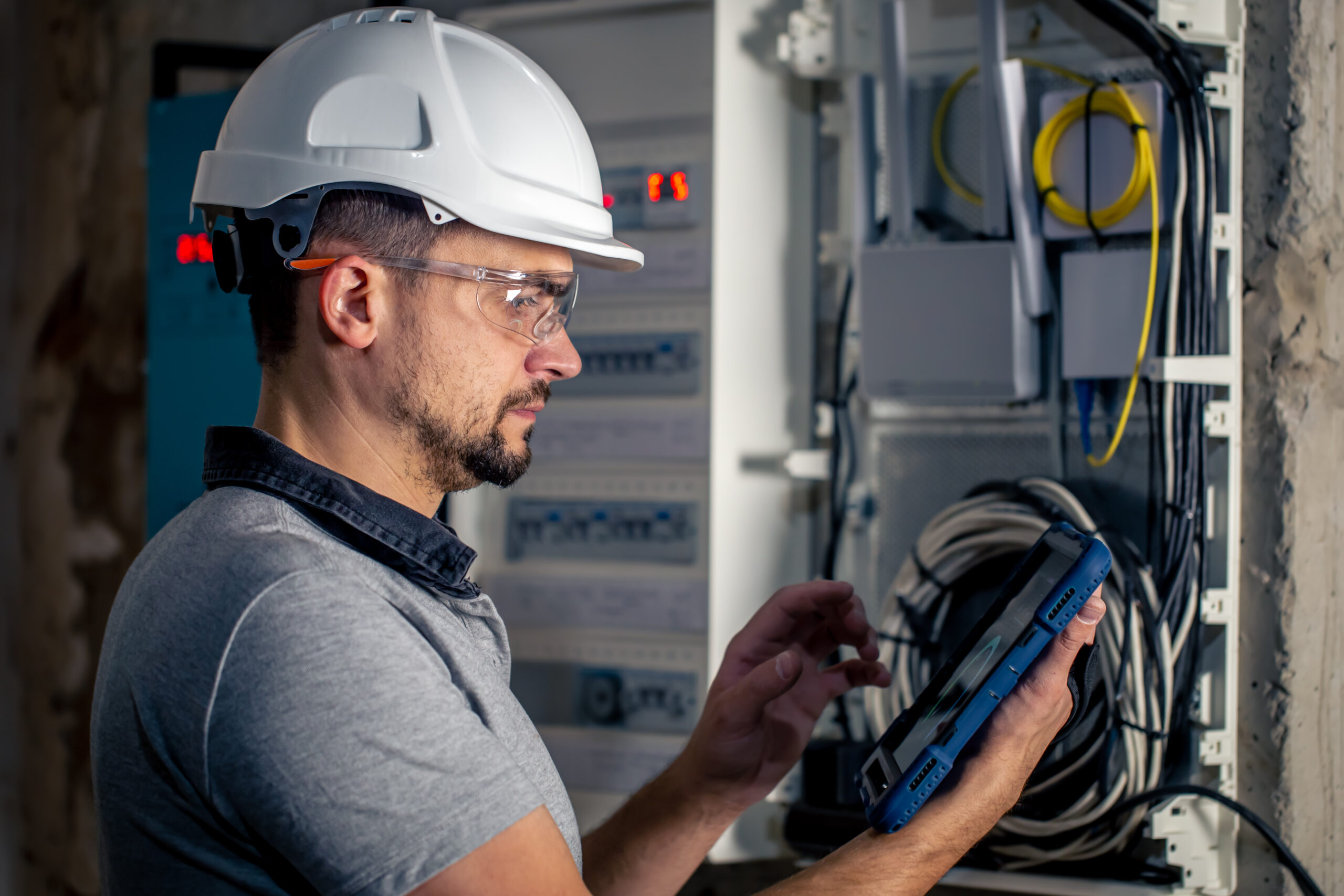 Man, an electrical technician working in a switchboard with fuses. Installation and connection of electrical equipment. Professional uses a tablet.